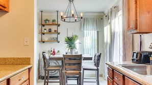 A kitchen with wooden cabinets, a dining table with chairs, a chandelier, and a window with curtains. - Bring Your Pet! Snowbird Haven w/ Community Pool! (Scottsdale)