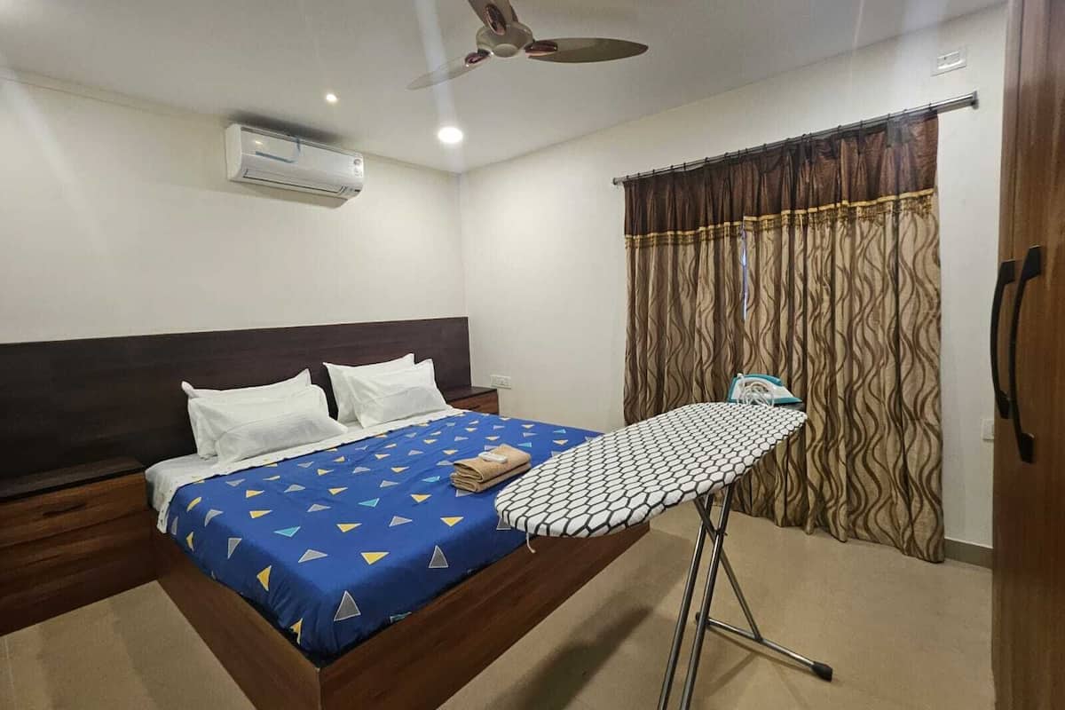 A hotel room with a bed, an ironing board, a ceiling fan, and curtains.