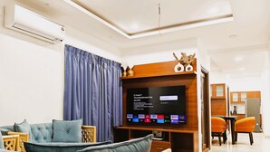 A modern living room with a flat-screen TV, a sofa, and a dining area with chairs. - Crescent Stays Banjara Hills  (Hyderabad)
