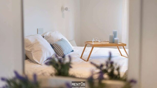 Een slaapkamer met een bed, kussens, een nachtkastje met kaarsen en een raam.