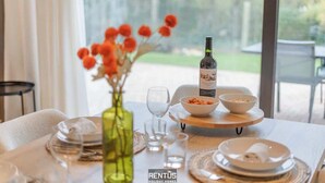 Een gedekte eettafel met borden, kommen en een fles wijn, met een bloemenvaas en uitzicht op de omgeving.