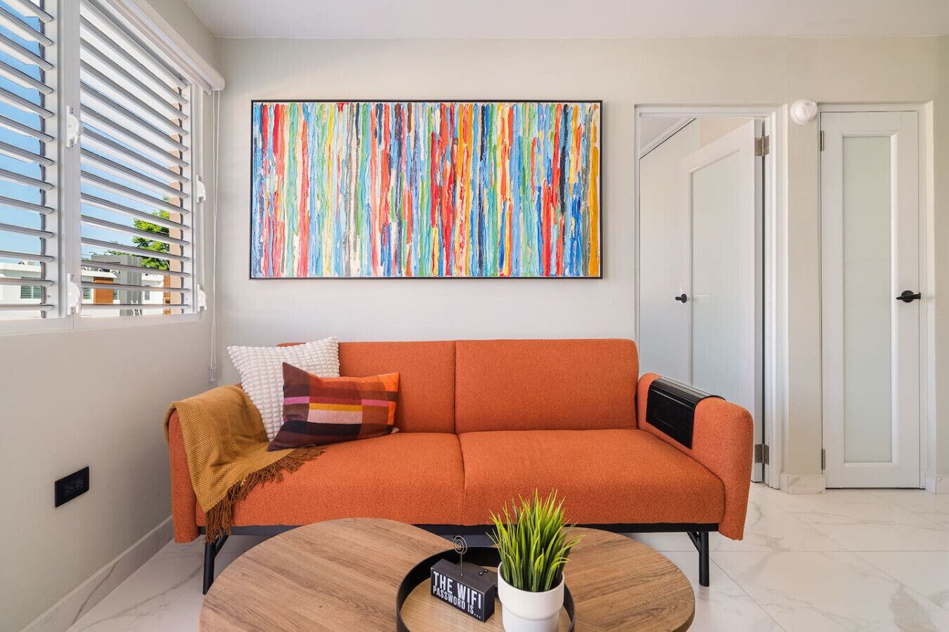 Een moderne woonkamer met een bank, een salontafel en een kleurrijk abstract schilderij.