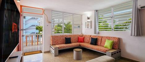 A living room with a sectional sofa, a TV, and a window with blinds.