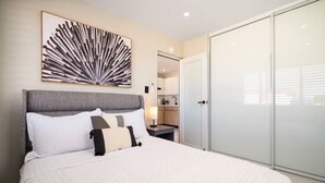 Quarto com cama grande, cabeceira, mesa de cabeceira com abajur, guarda-roupa e espelho.