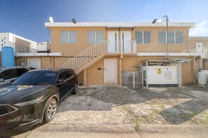 Un edificio a due piani con facciata beige, una scala che conduce al piano superiore e un'auto parcheggiata davanti.