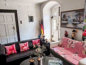 Un salon avec un canapé noir, une table basse, un jeu d’échecs et un tableau accroché au mur.