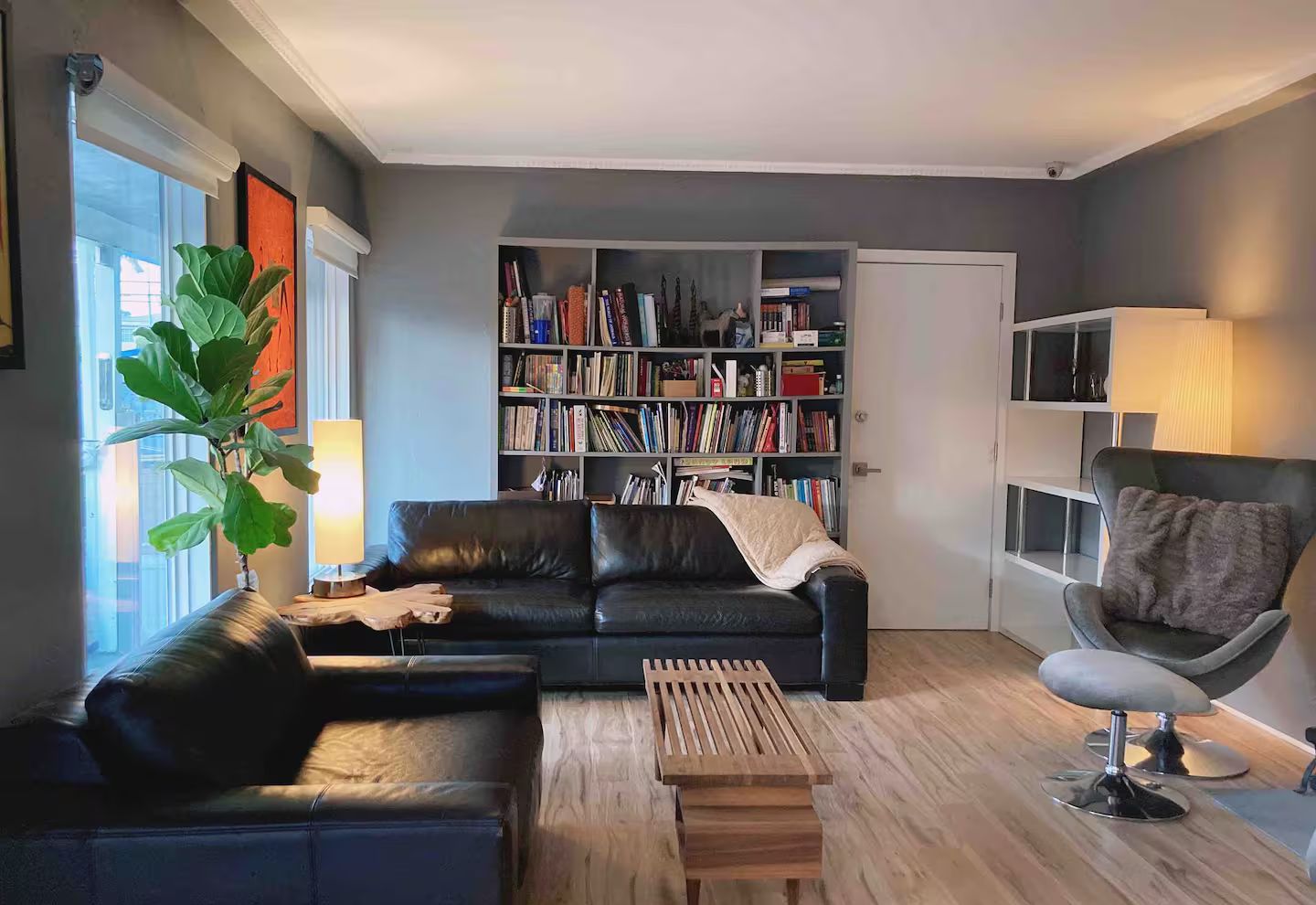 A modern living room with a black leather sofa, a wooden coffee table, a bookshelf filled with books, and a grey armchair.