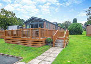 A wooden deck with a staircase leading to a building with large windows and a covered area. - 2 bedroom accommodation in Bala, (Bala,)