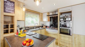 A modern kitchen with wooden cabinets, a central island with fruit, a built-in oven, and a stainless steel range. - 2 bedroom accommodation in Bala, (Bala,)