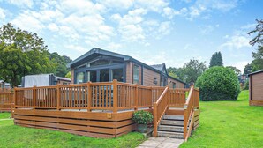 A wooden deck with a staircase leading to a building with large windows and a covered area. - 2 bedroom accommodation in Bala, (Bala,)