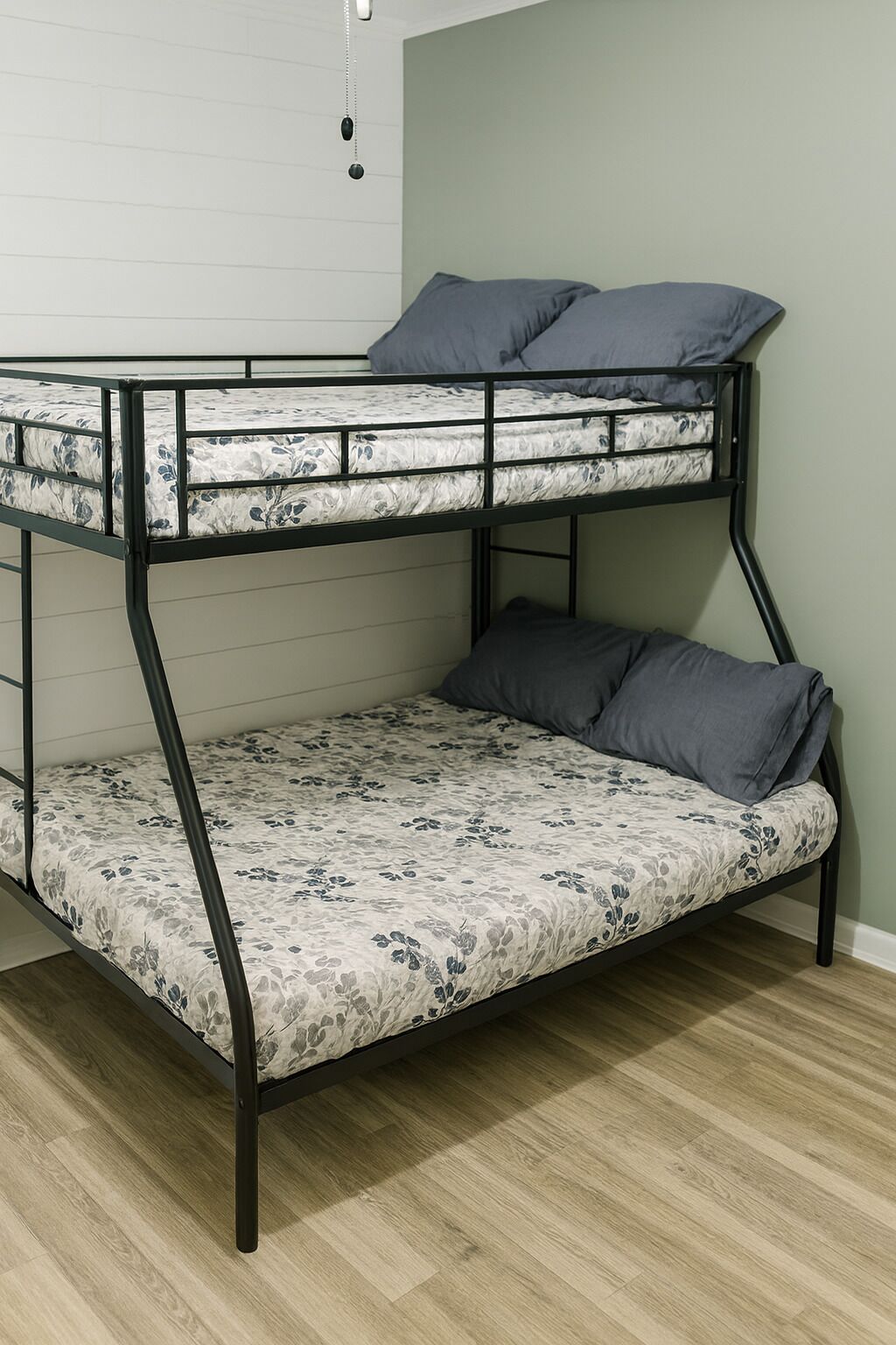 Ein Stockbett mit floralem Bettbezug, Metallgestell und grauem Kopfkissen.