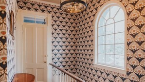 A hallway with patterned wallpaper, a wooden floor, a staircase with a white railing, and a large window. - Hawkins House - Historic Savannah Stay near Forsyth Park with Designer Interiors & Heated Pool (Savannah)