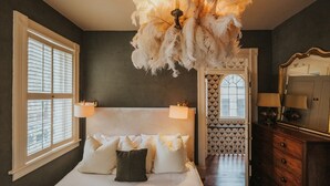A bedroom with a large bed, two bedside lamps, a chandelier, and a dresser with a mirror. - Hawkins House - Historic Savannah Stay near Forsyth Park with Designer Interiors & Heated Pool (Savannah)