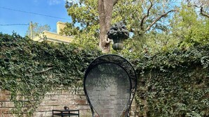 A checkered outdoor seating area with a metal chair and two lanterns, a brick wall, and a tree with a mushroom sculpture. - Hawkins House - Historic Savannah Stay near Forsyth Park with Designer Interiors & Heated Pool (Savannah)