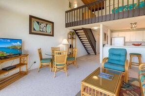 A living room with a TV, dining table, chairs, a sofa, a staircase, and a kitchen area. - Napili Point | Oceanfront 3 BR, Sleeps 10 | Car Incl. w/ 6+ Nights | NAP ML-2438 by KBM (Lahaina)