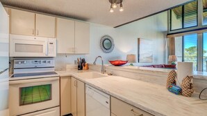 A modern kitchen with white cabinetry, a microwave, stove, and dishwasher. There is a window with a view of greenery outside. - Napili Point | Oceanfront 3 BR, Sleeps 10 | Car Incl. w/ 6+ Nights | NAP ML-2438 by KBM (Lahaina)