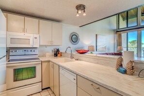 A modern kitchen with white cabinetry, a microwave, stove, and dishwasher. There is a window with a view of greenery outside. - Napili Point | Oceanfront 3 BR, Sleeps 10 | Car Incl. w/ 6+ Nights | NAP ML-2438 by KBM (Lahaina)