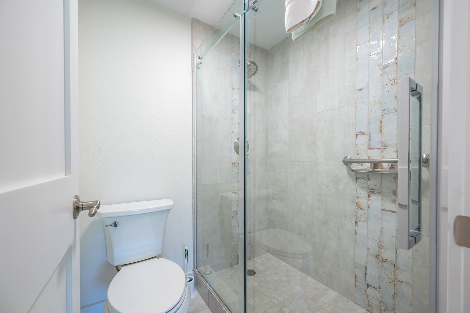A bathroom with a toilet, a glass-enclosed shower, and a tiled wall.