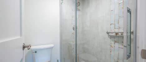 A bathroom with a toilet, a glass-enclosed shower, and a tiled wall.