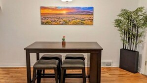 A dining area with a dark wooden table and three cushioned chairs. A painting of a sunset landscape hangs above the table. - Clean quiet and comfortable home welcomes you (Colorado Springs)