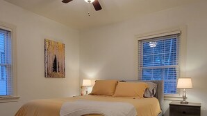 A bedroom with a bed, a ceiling fan, a nightstand, a lamp, a window with blinds, and a painting on the wall. - Clean quiet and comfortable home welcomes you (Colorado Springs)