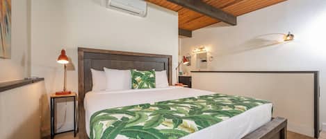 A bedroom with a bed, a ceiling fan, a wall-mounted air conditioner, a bedside lamp, and a nightstand.