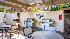 Un patio al aire libre con una parrilla, mesas, sillas y un reloj en la pared.