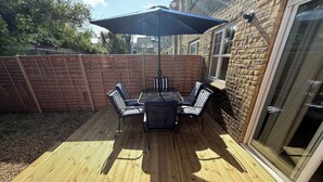 A wooden deck with a table and chairs, a brick wall, and a glass door. - 3 bed house with parking near Tower Bridge (London)
