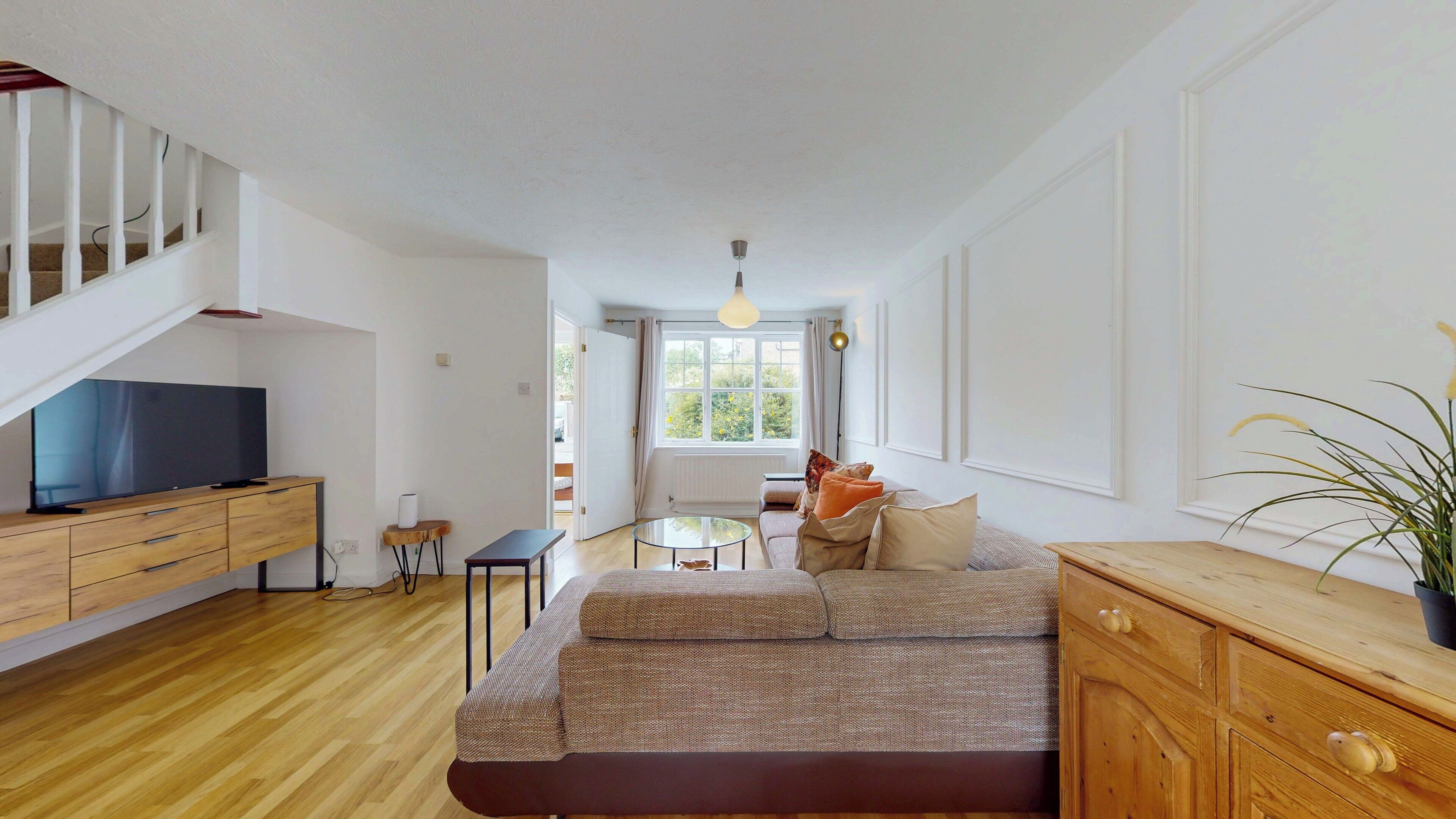 A modern living room with a sofa, a TV, a wooden cabinet, and a staircase.