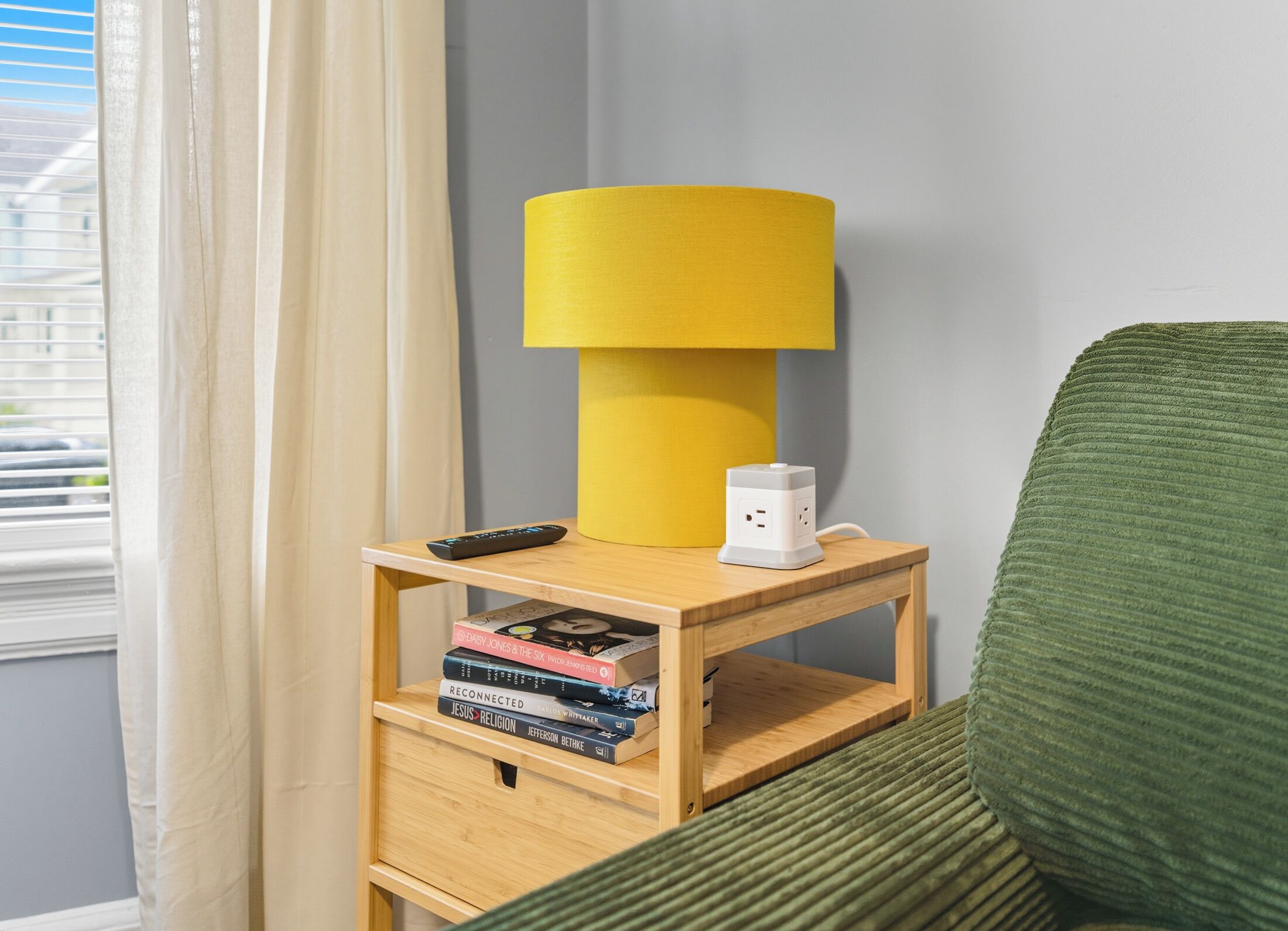 Ein Nachttisch aus Holz mit einer gelben Lampe, einer Fernbedienung und einem Stapel Bücher.