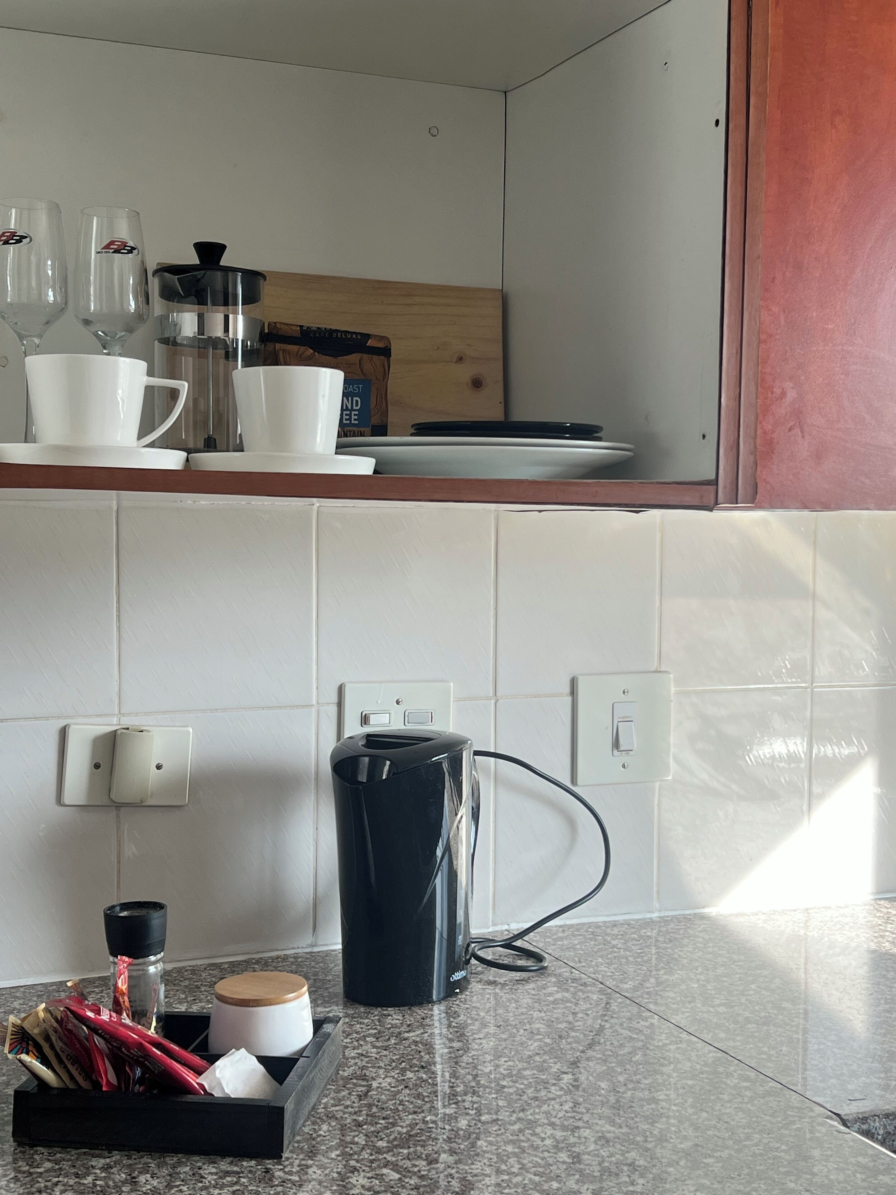 A kitchen with a coffee maker, cups, and a coffee grinder on the counter.