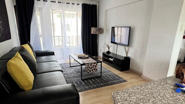 Ett modernt vardagsrum med en svart lädersoffa, ett mönstrat soffbord, en platt-TV och ett trägolv.