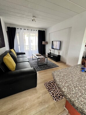 Ett modernt vardagsrum med en svart lädersoffa, ett mönstrat soffbord, en platt-TV och ett trägolv.
