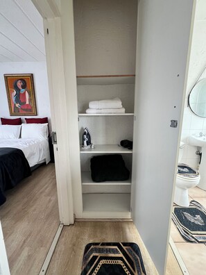 A hotel room with a bed, a closet with shelves, a bathroom with a toilet, and a painting on the wall. - Serene, Bryanston + free pizza (Sandton)