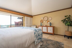 A bedroom with a bed, a dresser, a large window, and a plant.