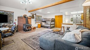 Een gezellige woonkamer met een open haard, een bank, een televisie en een keuken die door een open deur zichtbaar is.