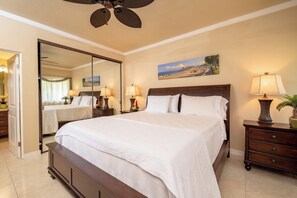 A hotel room with a large bed, a ceiling fan, a painting of a beach, and a nightstand with a lamp. - Kapalua Golf | Golf View 3 BR, Sleeps 9 | Car Incl. w/ 6+ Nights | KGV ML-2204 by KBM (Lahaina)