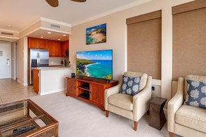 A living room with a TV, a sofa, a chair, a coffee table, and a kitchen area. - Kapalua Golf | Golf View 3 BR, Sleeps 9 | Car Incl. w/ 6+ Nights | KGV ML-2213 by KBM (Lahaina)