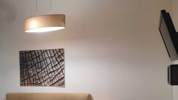 A modern hotel room with a bed, a desk, a chair, a lamp, and a wall-mounted TV. - Charming 1BR Apartment In Top Location (Vienna)