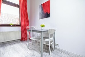A modern room with a white table and chairs, a window with red curtains, a radiator, and a wall-mounted abstract painting. - Bright 1BR Apartment in Central Vienna (Vienna)