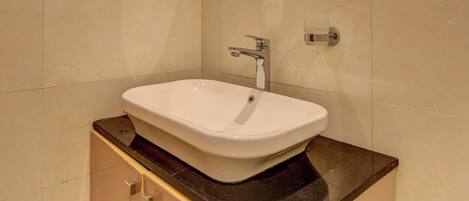 Un baño con un lavabo blanco, un espejo redondo y paredes de cerámica beige.