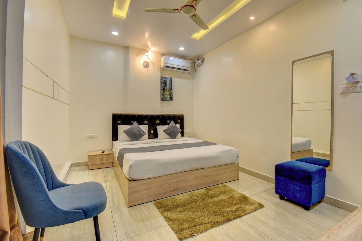 A modern bedroom with a bed, a chair, a small table, a mirror, and an air conditioning unit.