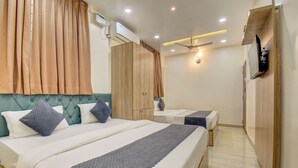 A hotel room with a large bed, a smaller bed, a wardrobe, a TV, and a ceiling fan. - Le Mysuru Palace (Mysore)