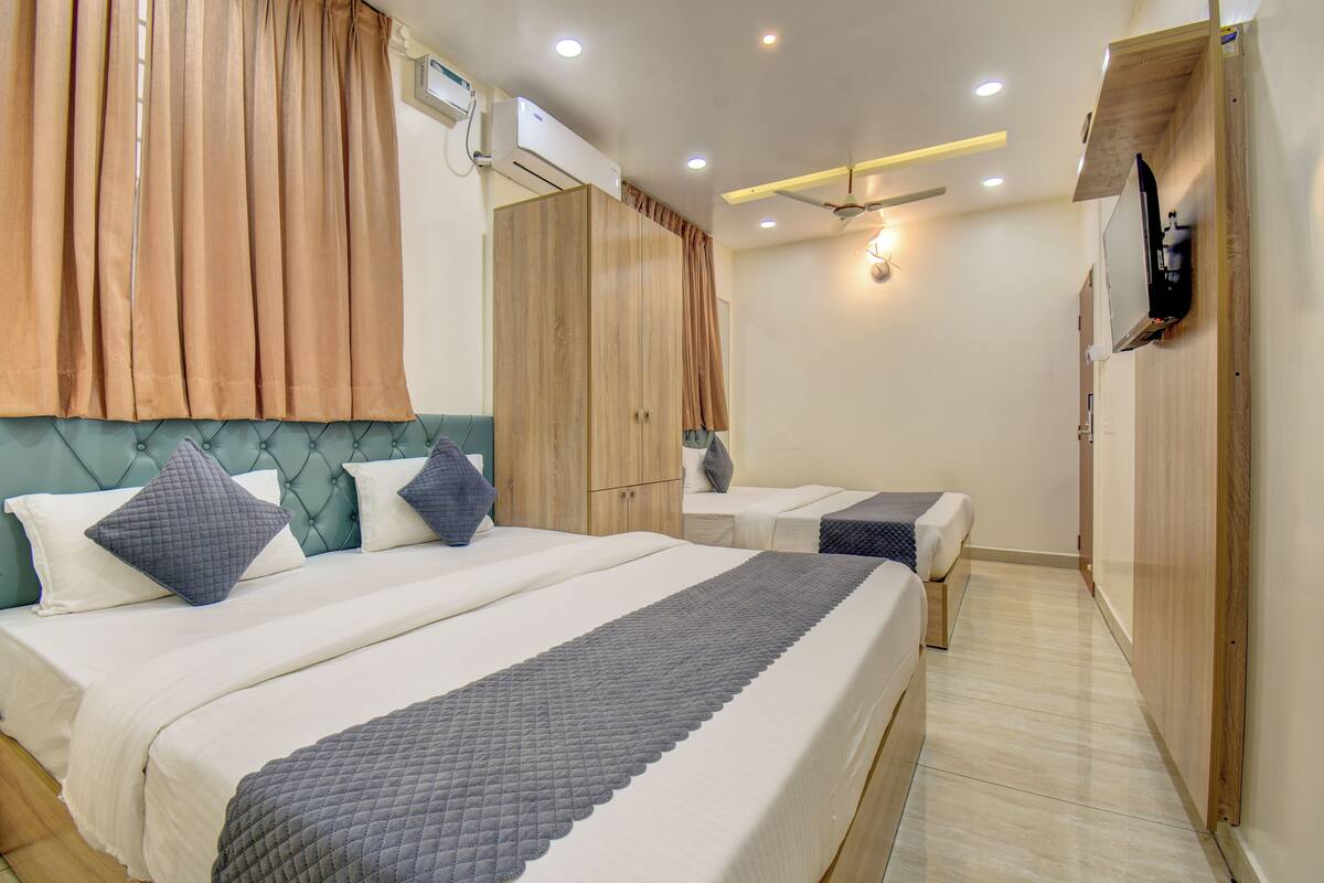 A hotel room with a large bed, a smaller bed, a wardrobe, a TV, and a ceiling fan.