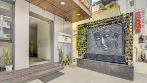 A hotel entrance with a Buddha statue, potted plants, and a sign for "Rooms AC & Non AC". - Le Mysuru Palace (Mysore)
