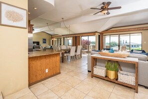 A spacious kitchen with a wooden island, dining area with chairs, a sofa, and a large window offering a view. - Kapalua Golf | Golf View 3 BR, Sleeps 9 | Car Incl. w/ 6+ Nights | KGV ML-2219 by KBM (Lahaina)