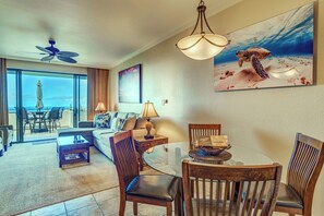 A hotel room with a balcony, a dining area, a sofa, a table, and a painting of a sea turtle. - Kapalua Golf | Golf View 3 BR, Sleeps 9 | Car Incl. w/ 6+ Nights | KGV ML-2219 by KBM (Lahaina)
