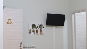 A room with a white door, a mounted TV, and a wall-mounted picture of potted plants. - La casetta di Fra & Giu (Longobucco)