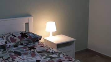 A bedroom with a bed, a nightstand with a lamp, and a small drawer unit.