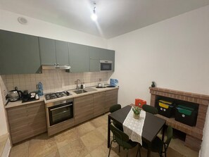 Une cuisine compacte équipée d’une cuisinière, d’un évier et d’un four à micro-ondes. On y trouve une table à manger avec des chaises et une petite plante en pot.